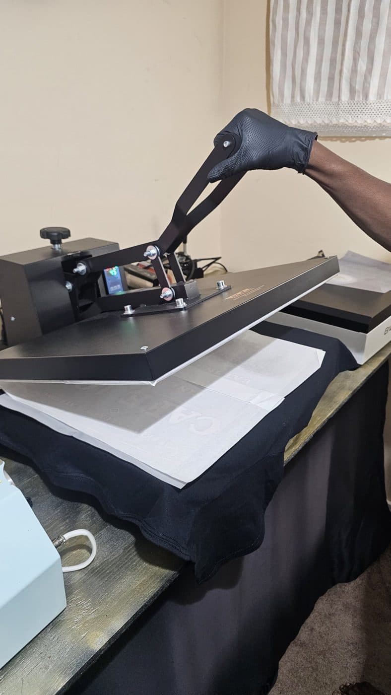 A gloved hand lifting our heat press after pressing a black tee in Edison, NJ