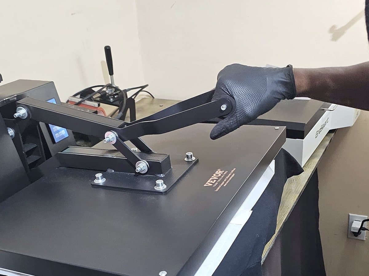 A gloved hand pulling our heat press down onto a black tee