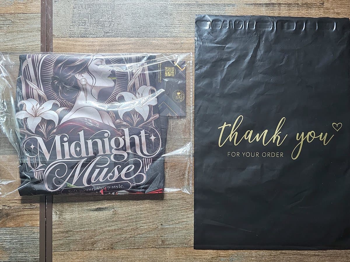A folded Midnight Muse tee sealed in a sleeve next to a black “thank you” mailer